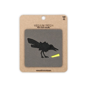 May include: A medium-sized patch with hook velcro, featuring a black crow silhouette and a yellow accent. The patch is on a gray background, mounted on a cardboard backing. Text includes "MEDIUM PATCH" and "MADE IN USA".