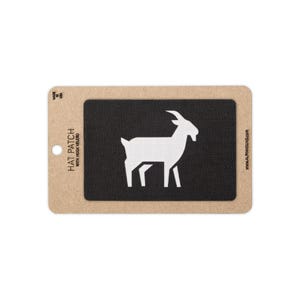 May include: A rectangular black fabric hat patch featuring a white silhouette of a goat. The patch is mounted on a tan cardboard backing with the text "HAT PATCH WITH HOOK VELCRO" printed on the left and "MADE IN USA" at the top left corner.