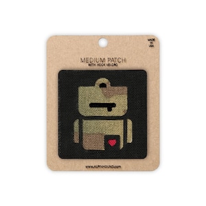 May include: A medium patch with hook velcro featuring a robot design in camouflage colors. The patch is on a black background and is attached to a cardboard backing. The text "MEDIUM PATCH WITH HOOK VELCRO" is printed on the backing.