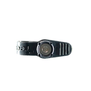 May include: A black metal clasp with a silver circular center and a ridged handle. The word "Free" is embossed on the side of the clasp. The clasp is designed to secure an item.