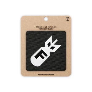 May include: A black medium patch with hook velcro featuring a white graphic of a bomb with the letter "F". The patch is on a brown cardboard backing with the text "MEDIUM PATCH WITH HOOK VELCRO" and "MADE IN USA". The website address is also visible.