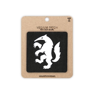 May include: A black square patch featuring a white silhouette of an anteater. The patch is mounted on a tan cardboard backing labelled MEDIUM PATCH WITH HOOK VELCRO, MADE IN USA, and the website address WWW.ALPINHOUND.COM at the bottom.