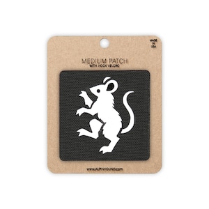 May include: A square black patch featuring a white silhouette of a standing mouse. The patch is mounted on a rectangular brown cardboard backing labelled MEDIUM PATCH WITH HOOK VELCRO and WWW.ALPINHOUND.COM with MADE IN USA printed at the top.