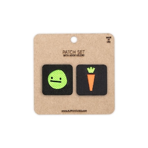 May include: A patch set with hook velcro. The set includes two black square patches. One patch features a lime green circle with a black horizontal line and two dots. The other patch has an orange carrot with a green top. The text "PATCH SET WITH HOOK VELCRO" is printed on the card.