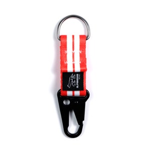 Pu&ograve; includere: Portachiavi a strisce rosse e bianche con un moschettone in metallo nero e un logo in bianco e nero che dice "ALPINIHOUND  P.E.T.C."
