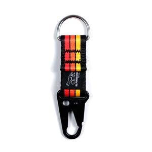 Pu&ograve; includere: Un portachiavi nero con un cinturino a strisce rosse, arancioni e gialle e un moschettone nero. Il cinturino ha il testo "ALPINIHOUND" e un piccolo logo di lupo.