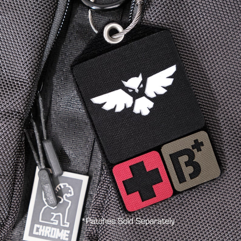 May include: A black luggage tag with a white owl logo, a red patch with a white cross, and a brown patch with a white "B+" logo. The text "*Patches Sold Separately" is printed below the patches.