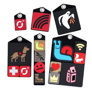 May include: A set of eight black and white fabric patches with various colorful designs. The patches feature a rainbow, a ghost, a dog, a snail, a dragonfly, a smiley face, a heart, a crown, a milk carton, a squirrel, and a wifi symbol.