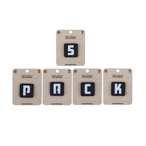 May include: Five iron-on patches with white letters on a black background. The patches spell out "PACK" and include the number "5".