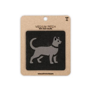 May include: A medium-sized, black patch with hook and loop fastening, featuring a grey silhouette of a dog. The patch is on a cardboard backing with the text "MEDIUM PATCH WITH HOOK VELCRO". The website address www.alpinhound.com is printed at the bottom.