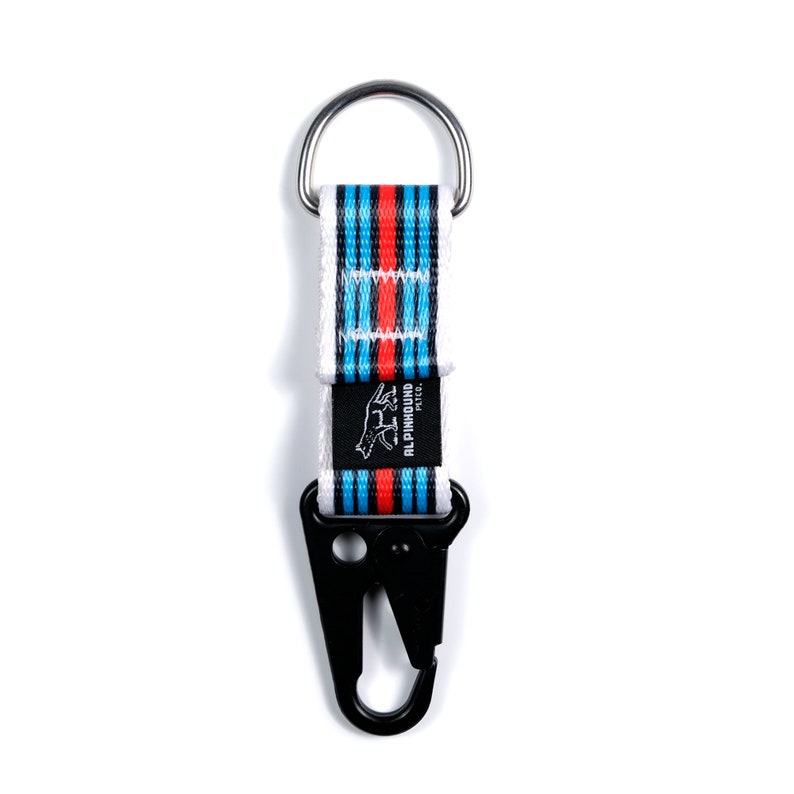 Pu&ograve; includere: Un portachiavi a strisce bianche e blu con un moschettone nero. Il portachiavi ha un anello argentato e un patch con logo nero che dice "ALPINHOUND PET CO."