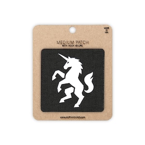 May include: A black square patch featuring a white silhouette of a rearing unicorn. The patch is mounted on a tan cardboard backing labeled MEDIUM PATCH WITH HOOK VELCRO and WWW.ALPINHOUND.COM, with MADE IN USA printed in the top right corner.