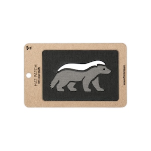 May include: A rectangular black hat patch with a hook velcro backing, featuring a grey and white honey badger graphic. The patch is mounted on a tan cardboard display card with the text HAT PATCH WITH HOOK VELCRO, MADE IN USA, and ALPINHOUND.COM.