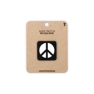 May include: A black square mini patch with a white peace symbol, attached to a brown cardboard backing. The text "MINI PATCH WITH HOOK VELCRO" is printed above the patch. The website address www.alpinhound.com is printed below the patch.