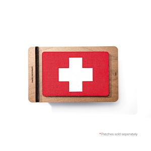May include: A red and white Swiss flag patch featuring a white cross on a red background, presented on a wooden base. The text "ALPHAHOUND SUPPLY" is printed vertically on the left. "USA" is printed on the right.