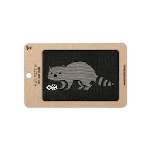 May include: A rectangular black hat patch with a hook velcro backing, featuring a gray raccoon graphic and a white fish skeleton icon. The patch is mounted on a tan cardboard display card with the text HAT PATCH WITH HOOK VELCRO and MADE IN USA.