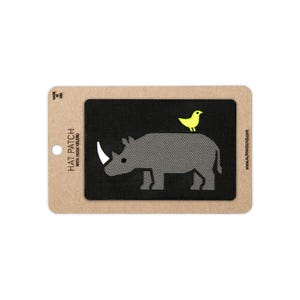May include: A rectangular black patch featuring an embroidered gray rhinoceros with a white horn and a small yellow bird perched on its back. The patch is mounted on a tan cardboard backing labeled HAT PATCH WITH HOOK VELCRO.