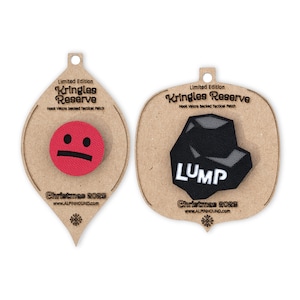 May include: Two Christmas ornaments shaped like teardrops with brown cardboard backing. The ornaments feature a red patch with a frowning face and a black patch with a gray rock and the word "LUMP" in white text. Both ornaments have the text "Limited Edition Kringles Reserve Hook Velcro backed Tactical Patch Christmas 2023 www.ALPINHOUND.com".