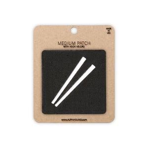 May include: A medium-sized black patch with hook velcro, featuring two white strips. The patch is mounted on a cardboard backing with the text "MEDIUM PATCH WITH HOOK VELCRO" and "MADE IN USA". The website address www.alpinhound.com is printed at the bottom.