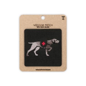 May include: A black medium patch with hook velcro featuring a white and gray dog design with a red cross emblem. The patch is on a cardboard backing with the text "MEDIUM PATCH WITH HOOK VELCRO" and "MADE IN USA". The website www.alpinhound.com is also visible.