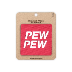 May include: A square red fabric patch with white text that reads PEW PEW. The patch is mounted on a rectangular tan cardboard backing card that features the text MEDIUM PATCH WITH HOOK VELCRO, MADE IN USA, and the website URL ALPINHOUND.COM.