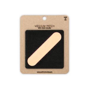 May include: A medium-sized patch with hook velcro, featuring a black square with a beige, elongated oval shape. The patch is on a cardboard backing with the text "MEDIUM PATCH WITH HOOK VELCRO" and "MADE IN USA". The website address www.alpinhound.com is also visible.