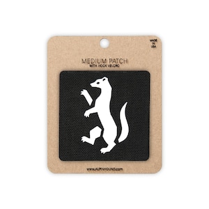 May include: A square black patch with a white silhouette of a standing animal, labeled MEDIUM PATCH WITH HOOK VELCRO and WWW.ALPINHOUND.COM on a tan cardboard backing with a hole at the top, marked MADE IN USA.