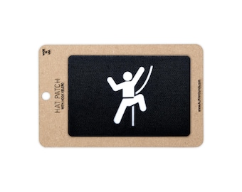 May include: A rectangular black hat patch with a white graphic of a person climbing a rope. The patch is mounted on a tan cardboard backing with the text HAT PATCH WITH HOOK VELCRO, MADE IN USA, and ALPHAHOUND.COM printed on the sides.
