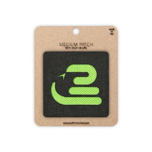 May include: A square black patch featuring a bright lime green stylised snake graphic. The patch is mounted on a rectangular tan cardboard backing labelled MEDIUM PATCH WITH HOOK VELCRO, MADE IN USA, and the website address WWW.ALPINHOUND.COM.