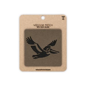 May include: A medium-sized patch with hook velcro featuring a black silhouette of a pelican in flight. The patch is on a brown background with the text "MEDIUM PATCH WITH HOOK VELCRO" and "MADE IN USA". The website address www.alpinhound.com is also visible.