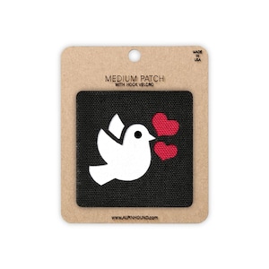 May include: A medium patch with hook and loop fastening. The patch shows a white dove with two red hearts on a black background. It is on a brown card with the text "MEDIUM PATCH WITH HOOK VELCRO" and "MADE IN USA". The website address is also visible.