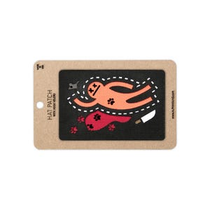 May include: A rectangular black hat patch with hook velcro backing on a cardboard display card. The patch features an orange gingerbread-style figure with X-shaped eyes, a red puddle, paw prints, and a white knife graphic with dashed lines.