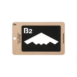 May include: A rectangular black hat patch with hook velcro backing, featuring a white B2 bomber aircraft silhouette and the text B2. The patch is mounted on a tan cardboard display card with the text HAT PATCH WITH HOOK VELCRO and MADE IN USA.