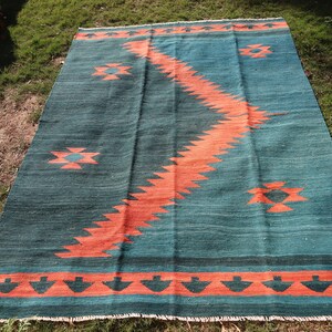 May include: A teal and orange handwoven rug with a geometric pattern. The rug has a fringe border.