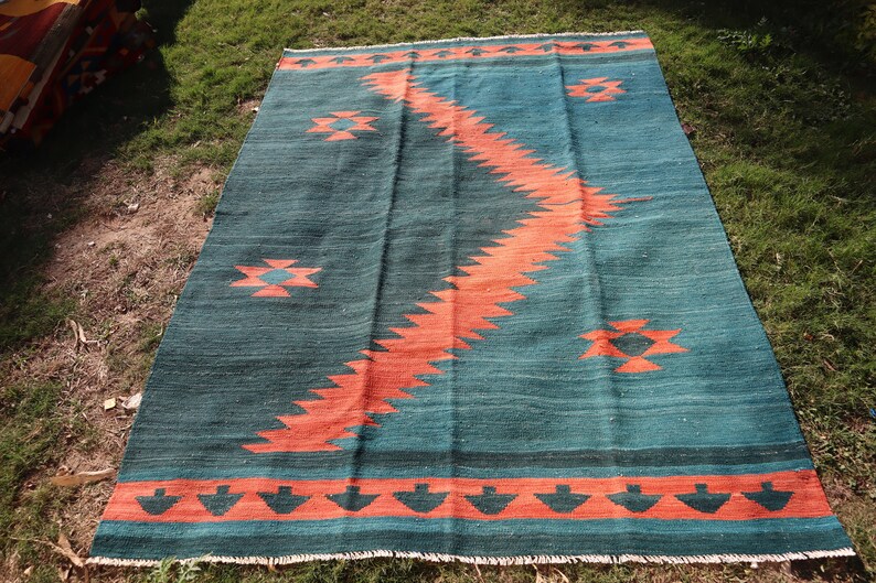 May include: A teal and orange handwoven rug with a geometric pattern. The rug has a fringe border.