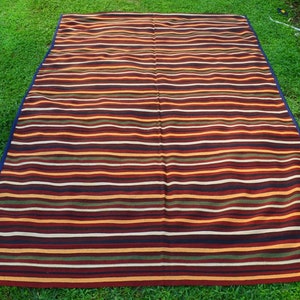 May include: A striped picnic blanket with a blue border. The blanket is made of a woven fabric and has a variety of colors, including red, orange, yellow, green, and brown.