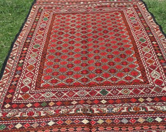 May include: A traditional red, black, and white patterned rug with intricate geometric designs. The rug has a thick, woven texture and a fringed edge.