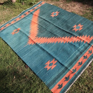 May include: A teal and orange patterned rug with geometric designs. The rug is laid out on a grassy surface.