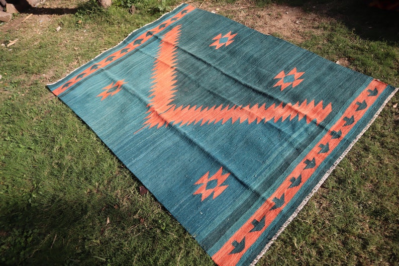 May include: A teal and orange patterned rug with geometric designs. The rug is laid out on a grassy surface.