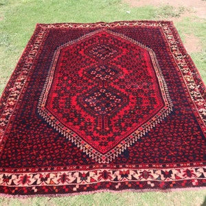 May include: A red and black rug with a geometric pattern. The rug has a fringed border and is made of wool.
