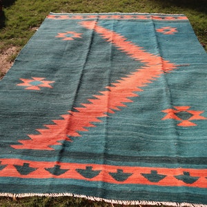 May include: A teal and orange geometric patterned rug with a fringed edge. The rug has a traditional design with a central diamond shape and a border of smaller diamonds.
