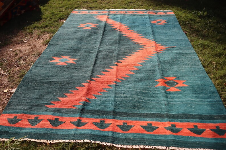 May include: A teal and orange geometric patterned rug with a fringed edge. The rug has a traditional design with a central diamond shape and a border of smaller diamonds.