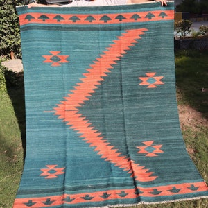 May include: A teal and orange handwoven rug with a geometric pattern. The rug has a fringe border and is made of wool.