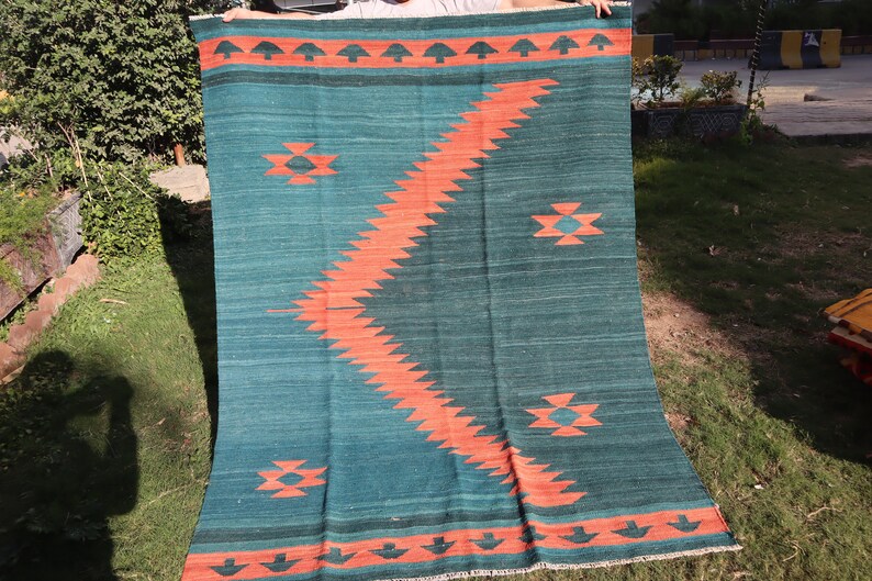 May include: A teal and orange handwoven rug with a geometric pattern. The rug has a fringe border and is made of wool.