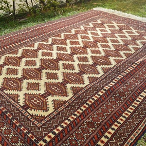 May include: A traditional rug with a geometric pattern in shades of red, brown, white, and black. The rug has a fringe border.