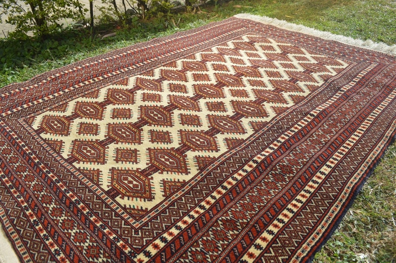 May include: A traditional rug with a geometric pattern in shades of red, brown, white, and black. The rug has a fringe border.