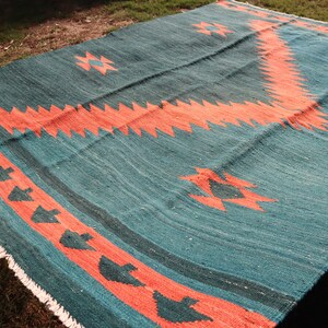 May include: A teal and coral rug with a geometric pattern. The rug has a fringe border and is made of woven wool.