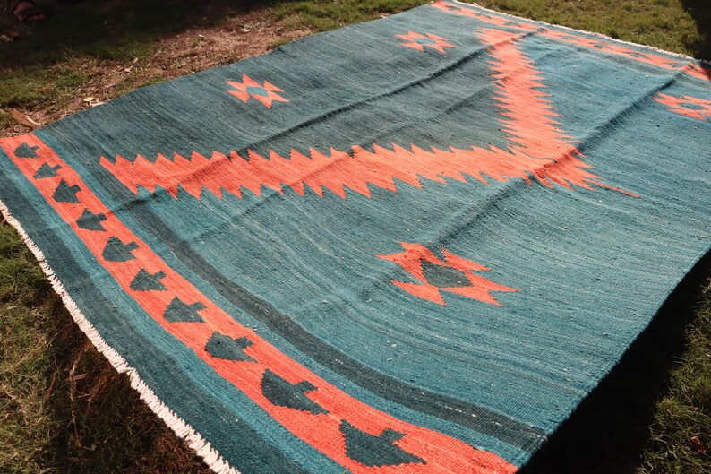 May include: A teal and coral rug with a geometric pattern. The rug has a fringe border and is made of woven wool.
