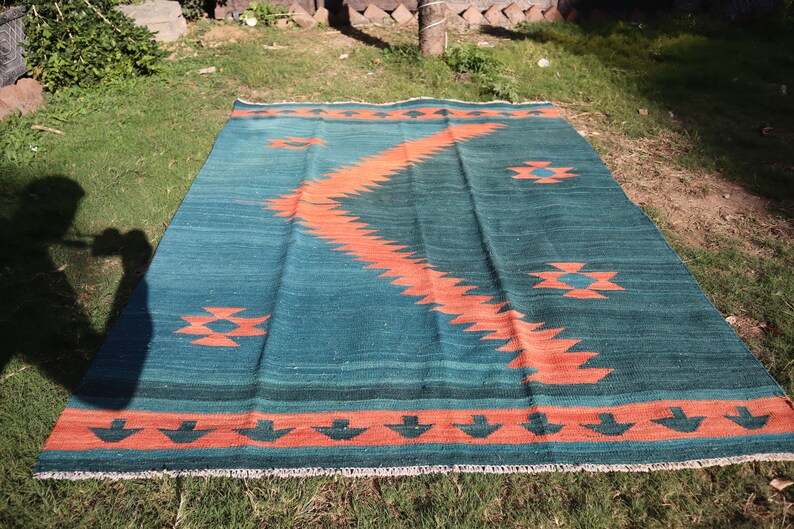 May include: A teal and orange patterned rug with a geometric design. The rug has a fringe border.