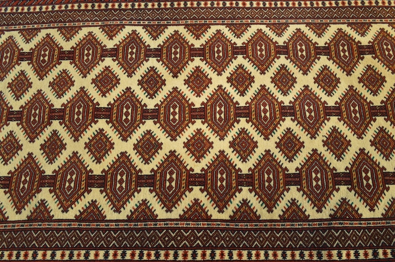 May include: A beige rug with a repeating geometric pattern in shades of red, brown, and green. The pattern features diamonds and hexagons.